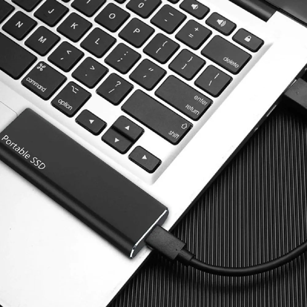 Bærbar USB-C ekstern harddisk på skrivebord med dokumenter, symboliserer sikker datakopi.