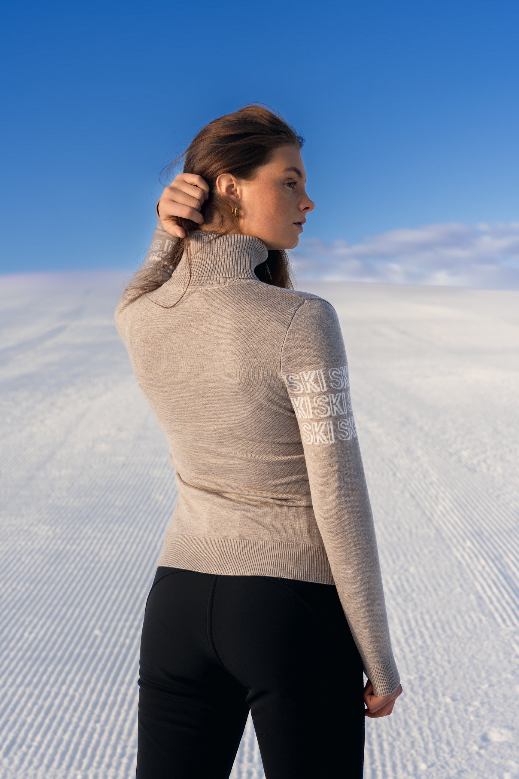 "Beige intarsia-strikket APRÈS-SKI genser for damer; ribbestrikket krage, varm og komfortabel til hyttetur og afterski."