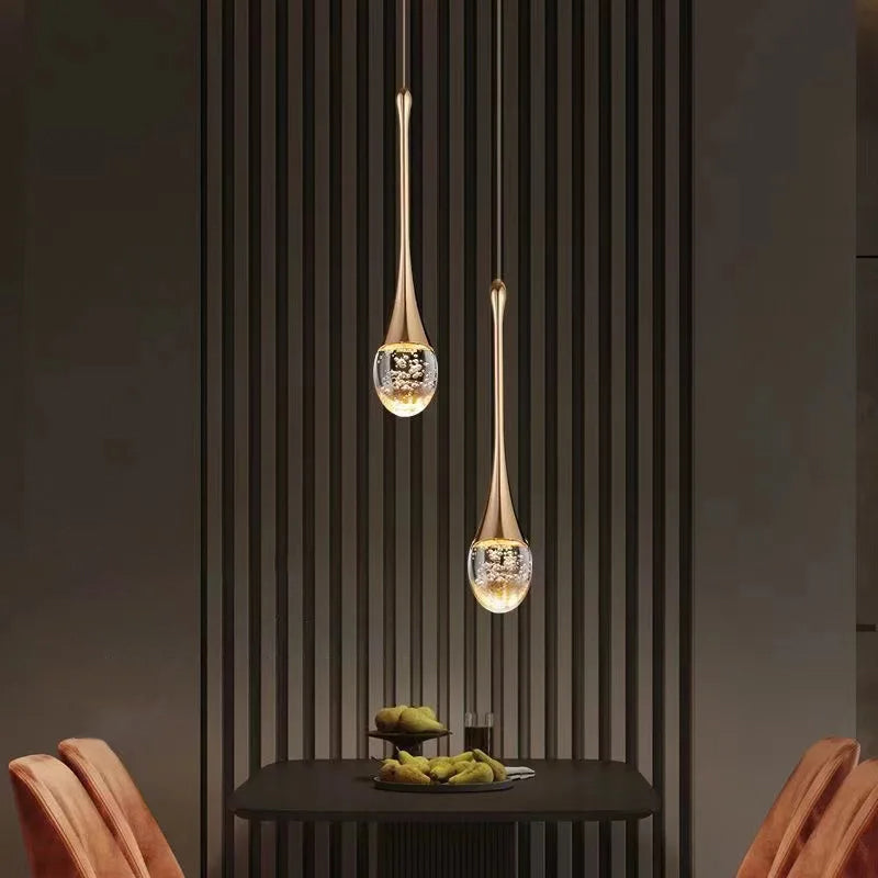 Dråpeformet taklampe i gull og svart, skaper elegant atmosfære i spisestuebelysning.
