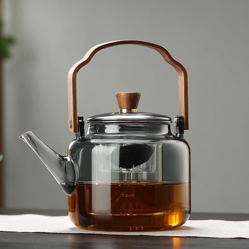 Gjennomsiktig glass tekanne med ergonomisk trehåndtak, ideell for å brygge og vise te.