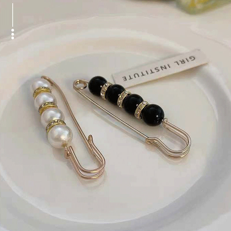 "Elegant sikkerhetsnålsbrosje med perler og rhinestones, perfekt for kjoler og skjerf, i svart og hvitt."