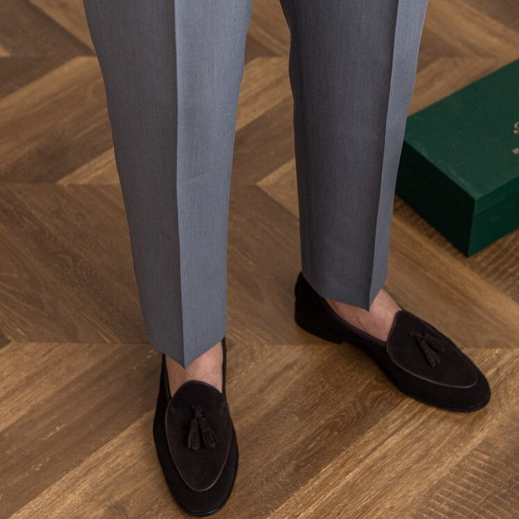 Mann poserer i mørke, skreddersydde høytliv herrebukser med plissert front; elegant formell look.