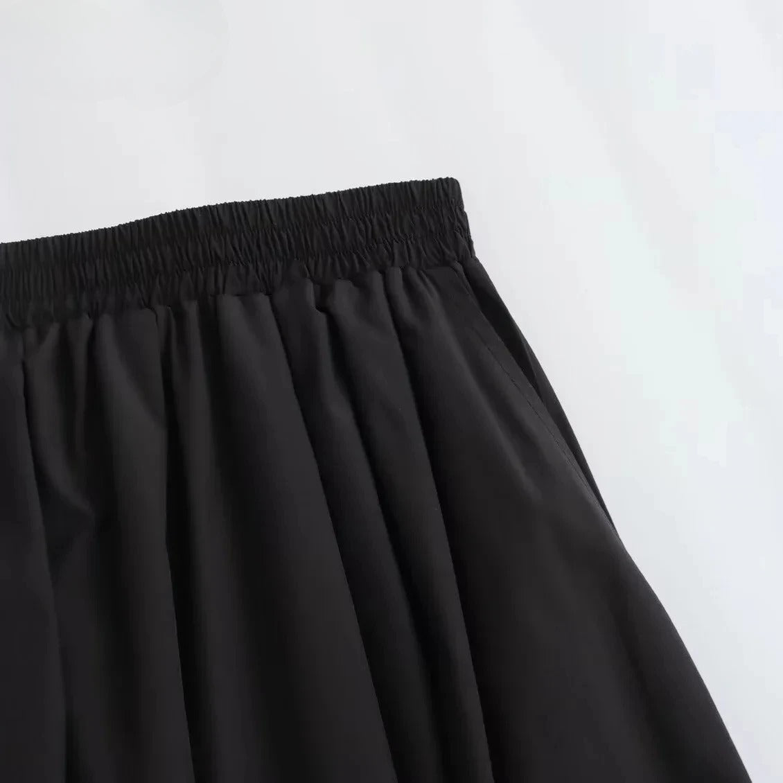Nærbilde av detaljene på det elegante, plisserte A-linje skjørtet i svart stoff.