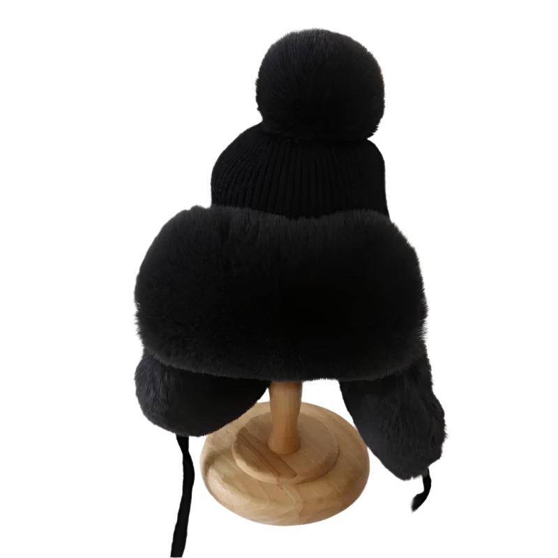 Nærbilde av trapper lue i beige, viser myke øreklaffer, pelskant og stor pompong, vintermote unisex.