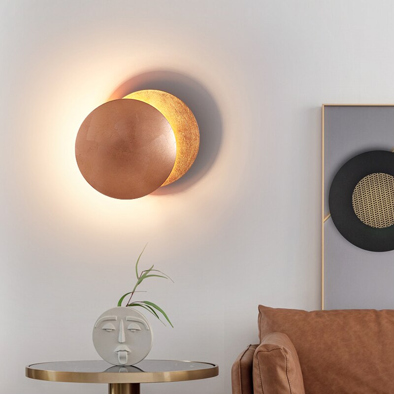 "Vegglampe med solformørkelseffekt, elegant design, to gylne roterende skiver, tilgjengelig i gull og kobber."