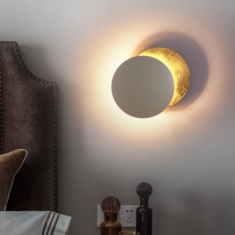 "Vegglampe med solformørkelseffekt, elegant design, to gylne roterende skiver, tilgjengelig i gull og kobber."