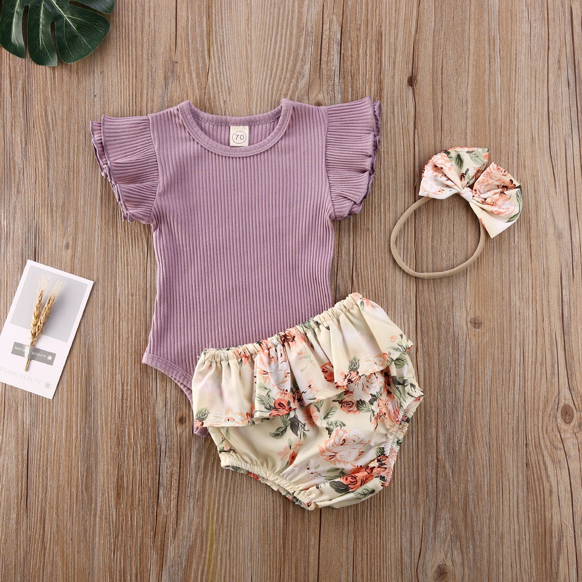 Ribbet babyjente sett med kortermet body, shorts med volanger og pannebånd, delikat blomsterdesign.