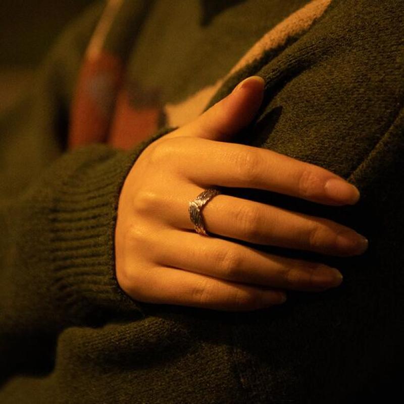 Unisex englevinge ring i sølv liggende på et mørkt trebrett, skaper kontrast rundt det beskyttende designet for smykker.