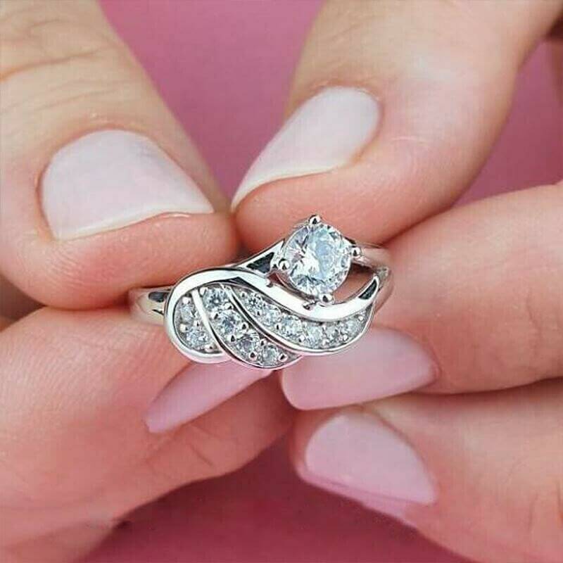 Gullfarget englevinge ring for kvinner, dekorert med glitrende cubic zirconia steiner. Symbolsk smykke.