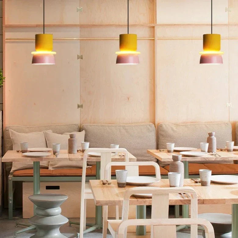 Moderne pendellampe i pastellrosa, henger over et spisebord for mykt lys
