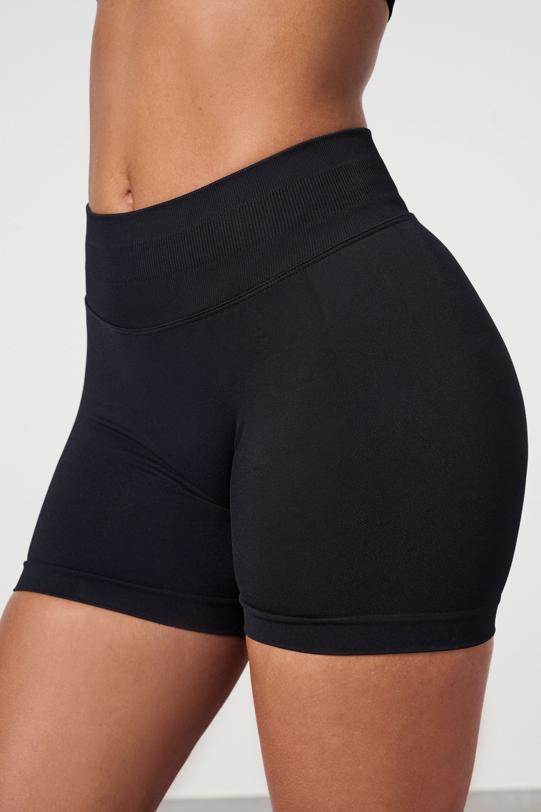 "Sømløse treningsshorts med scrunch-effekt for kurver, sort, sett forfra. Komfortabel med mid waist og 4-veis stretch."