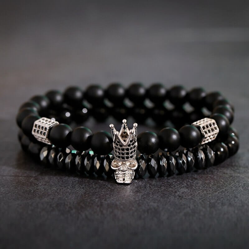 Nært bilde av unisex onyx armbånd med glinsende sorte perler og intrikat gullfarget krone sjarm. Beskyttende.