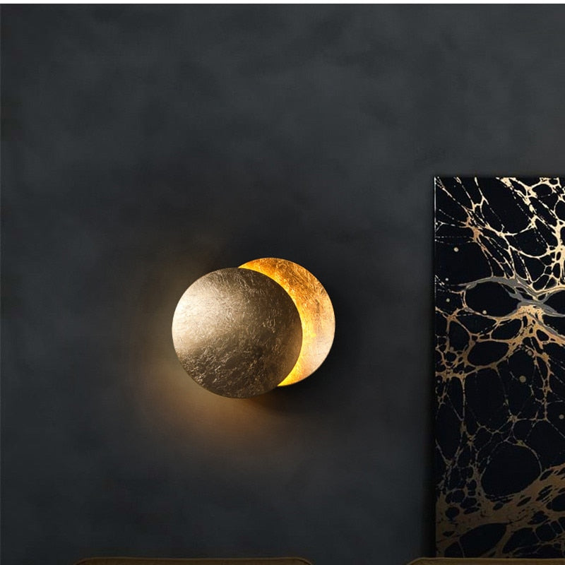 "Vegglampe med solformørkelseffekt, elegant design, to gylne roterende skiver, tilgjengelig i gull og kobber."