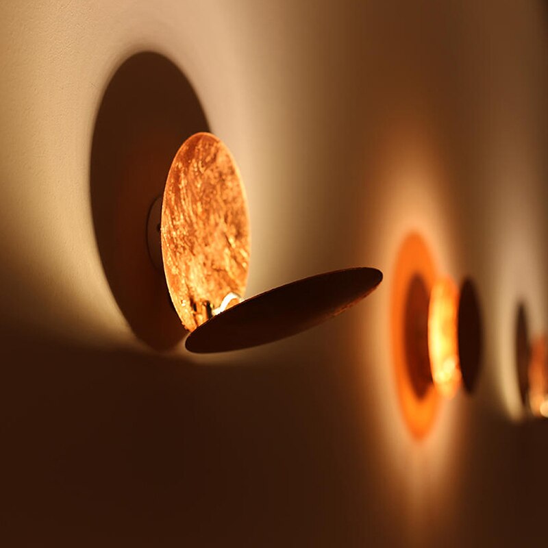 "Vegglampe med solformørkelseffekt, elegant design, to gylne roterende skiver, tilgjengelig i gull og kobber."